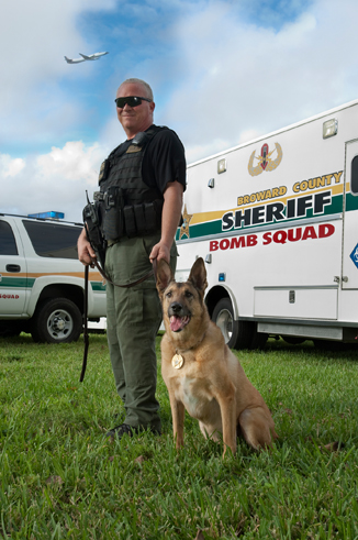 bomb squad man and his dog in front of truck with plane flying over